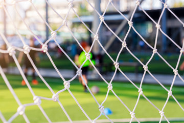 White mesh of goal with blurry football players.