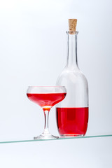 Wine glass and bottle with red alcoholic drink on a light gray background..