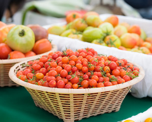 Detail on a market stall of fresh tomatoes, with focus on orange cherry tomatoes in the foreground. Organic food concept.