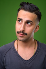 Young handsome Iranian man with mustache against green backgroun