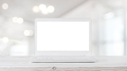 Laptop computer on wooden table in abstract blurred office interior