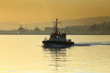 Fototapeta premium tug, sliding on the calm water of the Bay in the rays of the setting sun on the background of the port and mountains