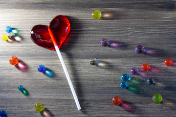 Red heart shape lollipop with lots of colorful candy sweets on grey wooden background, Love concept, Valentine’s day