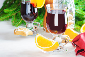 Mulled wine with cinnamon sticks in glass and cookies on wooden table with christmas tree branch on background