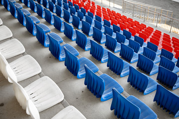 Empty white, red and blue rows of plastic seats on the concrete bases of the sports building, stadium