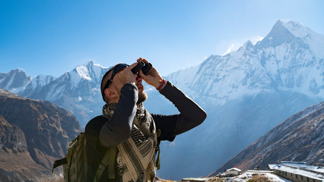Hiker looking through binoculars on a trekking trail to the Annapurna base camp, the Himalayas, Nepal. Himalayas mountain landscape in the Annapurna region. Snowy mountains, high peaks of Annapurna