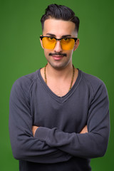 Young handsome Iranian man with mustache against green backgroun