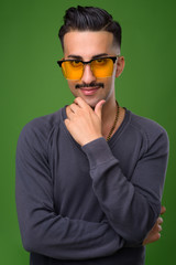 Young handsome Iranian man with mustache against green backgroun