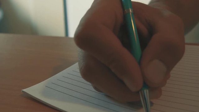 An inspirational short clip of a person's hand picking up a pen and start writing yearly goals. Motivation driven act of writing down your goals on a blank sheet.