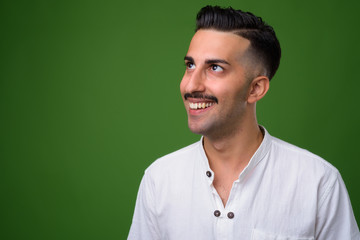 Young handsome Iranian man with mustache against green backgroun