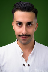 Young handsome Iranian man with mustache against green backgroun