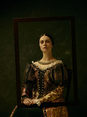 Portrait of a girl wearing a princess or countess dress over dark studio. portrait through picture...