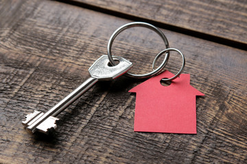The concept of buying a home. Keys with keychain house on a brown wooden background close-up.