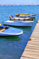Small boats moored at a wooden jetty on a bright blue sea