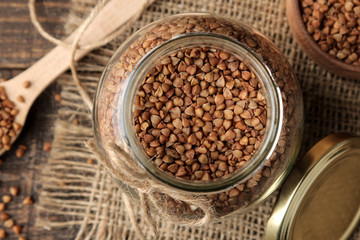 Dry buckwheat groats in a glass jar with a wooden spoon. top view on wooden brown table. cereals. healthy food. porridge.