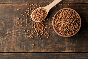 Dry buckwheat groats in a wooden bowl with a wooden spoon. top view on wooden brown table. cereals. healthy food. porridge.