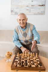 smiling senior man sitting on sofa and playing chess