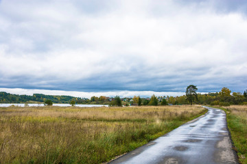 Fototapeta na wymiar Landscape with a river and a wet asphalt road on a cloudy autumn day.