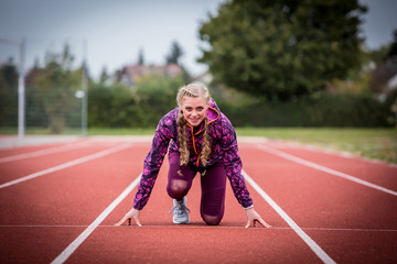 Junge Frau in Startposition auf einer Laufbahn