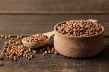 Dry buckwheat groats in a wooden bowl and spoon on a wooden brown table. cereals. healthy food....