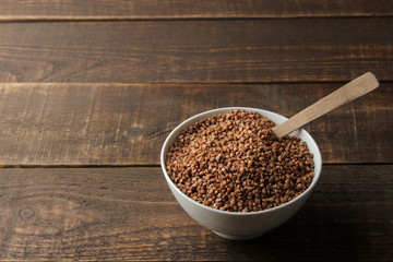 Dry buckwheat groats in a white bowl with a spoon on a wooden brown table. cereals. healthy food. porridge.