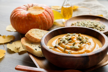 Pumpkin soup in a wooden bowl, with autumn leaves and pumpkin