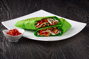 Shawarma in pita bread is cut and lies on a white plate. The Middle Eastern dish is prepared on the grill and served with sauce.