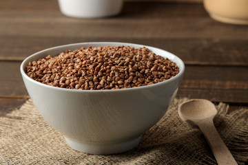 Dry buckwheat groats in a white bowl with a spoon on a wooden brown table. cereals. healthy food. porridge.