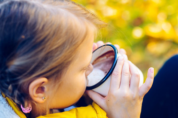 child girl drinking chocolate from a cup dressed in a warm yellow vest in autumn scenery