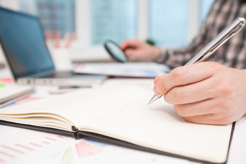 Businessman writes in a notebook while sitting at a desk.