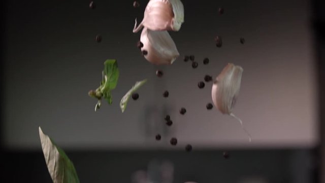 Garlic falling with pepper and leaves to wood cutting board, on kitchen background. Slow motion 480 fps. Sony rx 10