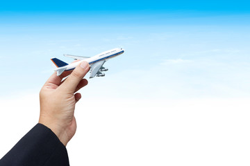 Business hand holding airplane against blue sky and cloud.