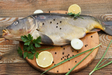 Raw carp with lemon, onion, pepper and parsley on cutting board on wooden table