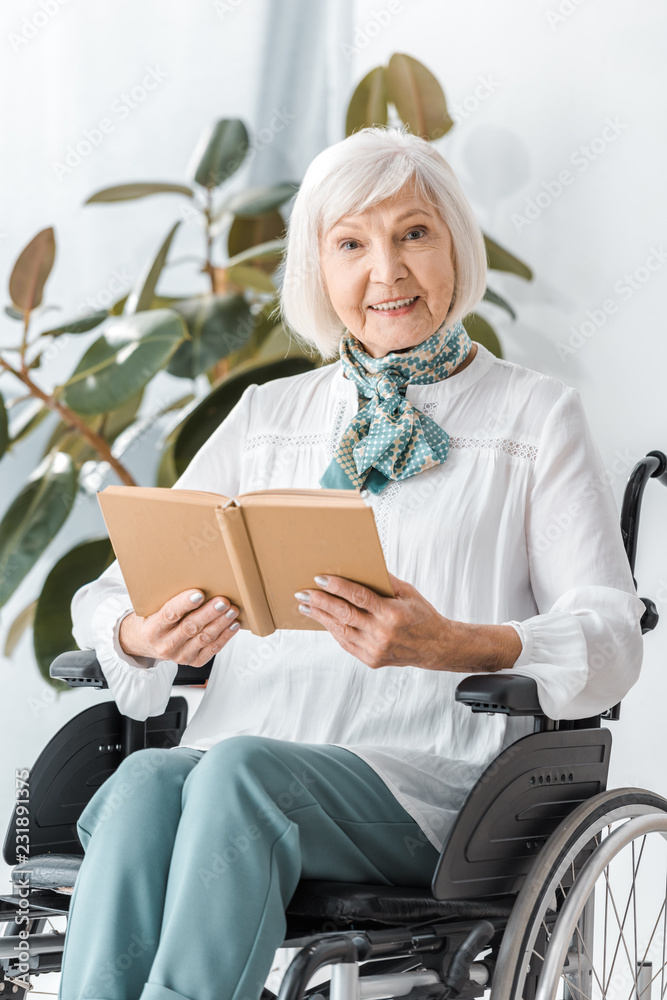 Wall mural happy senior woman sitting in wheelchair and reading book