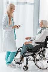 Obraz premium young female doctor writing prescription on clipboard to disabled senior woman