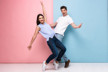 Full length image of excited man and woman in casual wear laughing and having fun together, isolated over colorful background