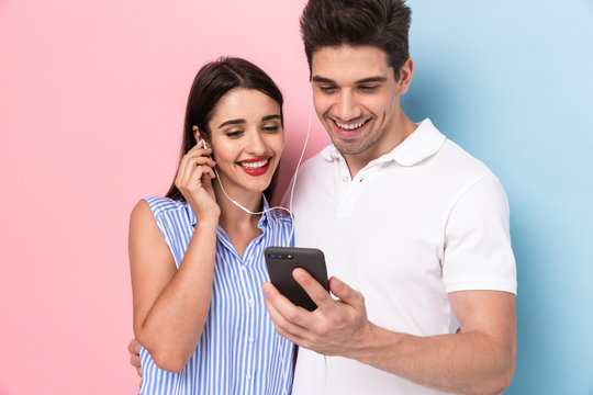 Image of lovely couple wearing earphones together and using smartphone, isolated over colorful background
