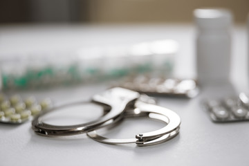 Handcuffs and pills and drugs on white table.