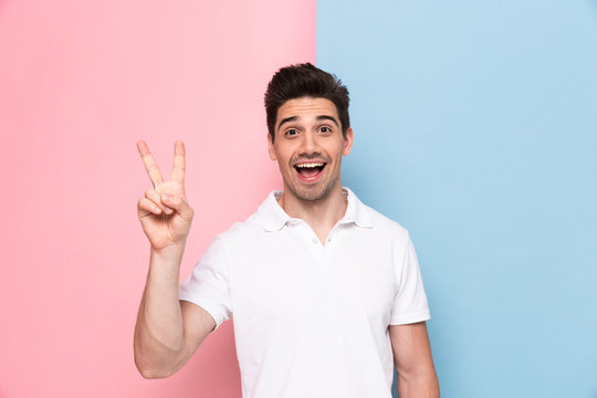 Image of positive man 30s having stubble showing peace sign with happy smile, isolated over colorful background