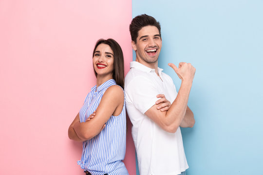 Image of young man and woman in casual wear standing back to back with arms crossed, isolated over colorful background