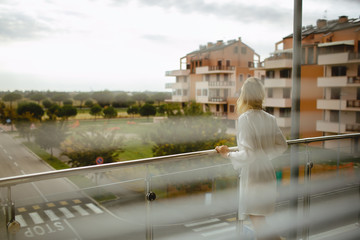 Back view of young girl dressed in bathrobe on balcony. Park outdoor background.