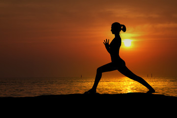 Fototapeta na wymiar Silhouette of woman practicing yoga on the beach at sunset