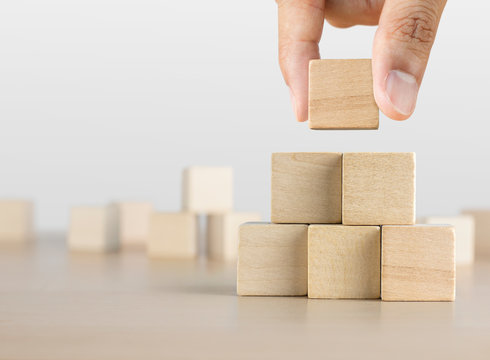 Hand arranging wooden blocks stacking as a pyramid staircase on white background. Success, growth, win, victory, development or top ranking concept.