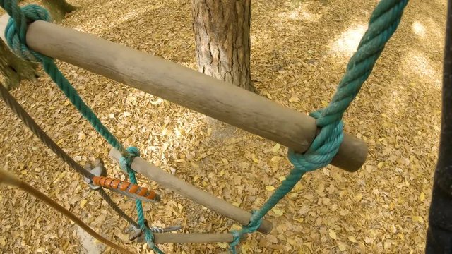 Person POV climbing on tree with rope ladder in adventure park ungraded 4K. Camera on a person's head with a wide view while climbing in adventure park in autumn. Slow motion first person view.