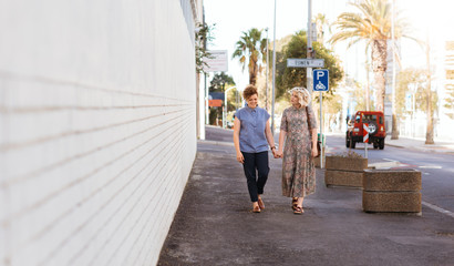 Smiling lesbian couple walking along a city sidewalk holding hands