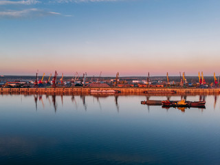 Port river cranes loading ships on barges delivery, sunset