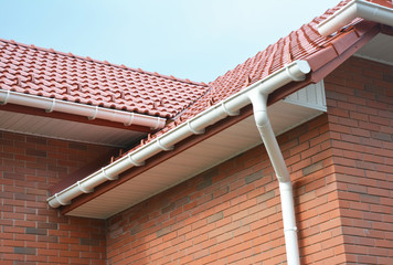 Rain gutter pipe system. Close up on Brick house with roof tiles and plastic roof gutter pipes...