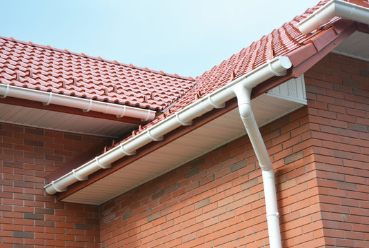 Rain gutter pipe system. Close up on Brick house with roof tiles and plastic roof gutter pipes drain. Guttering. Roofing construction problem area.