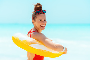 smiling young woman on beach wearing yellow inflatable lifebuoy