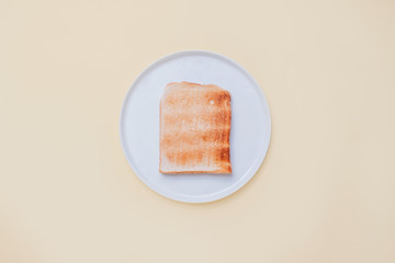 Top view of a plain slice of toast on a white plate on a vintage tan background with copy space and room for text.